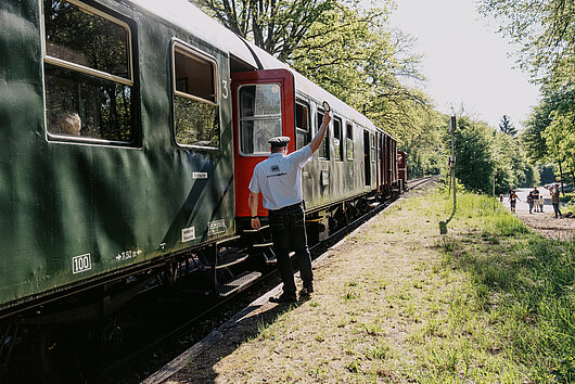 Der historische Museumszug steht an einem Bahnsteig. Der Zugführer gibt den Abfahrtsauftrag.